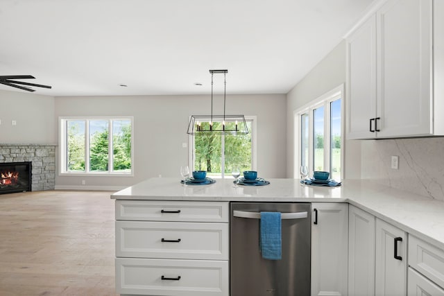 kitchen featuring white cabinetry, light wood-type flooring, pendant lighting, a stone fireplace, and dishwasher