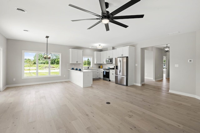unfurnished living room with baseboards, light wood-style flooring, ceiling fan with notable chandelier, and visible vents