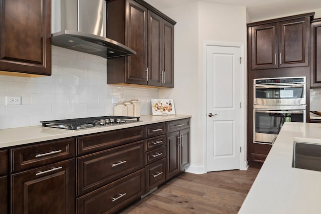 kitchen featuring dark hardwood / wood-style flooring, stainless steel appliances, dark brown cabinets, wall chimney exhaust hood, and tasteful backsplash