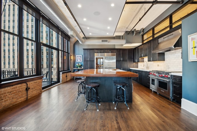 kitchen featuring wall chimney range hood, dark hardwood / wood-style flooring, a kitchen island, premium appliances, and a breakfast bar