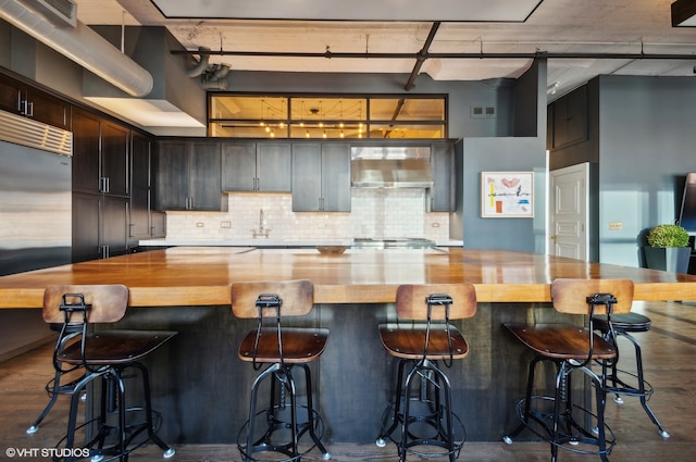 kitchen with wall chimney range hood, backsplash, wood-type flooring, and a kitchen bar