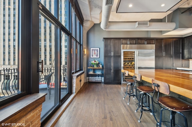 kitchen featuring dark hardwood / wood-style flooring, dark brown cabinets, wooden counters, built in refrigerator, and a breakfast bar