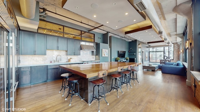 kitchen featuring light hardwood / wood-style flooring, wood counters, a kitchen island, tasteful backsplash, and a breakfast bar