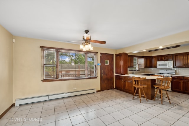 kitchen featuring white appliances, baseboard heating, kitchen peninsula, ceiling fan, and a breakfast bar area