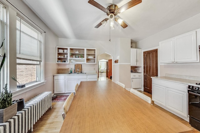 kitchen with ceiling fan, white cabinetry, electric range, radiator heating unit, and light hardwood / wood-style flooring