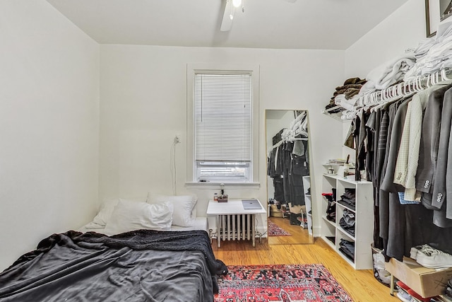 bedroom featuring hardwood / wood-style floors, ceiling fan, radiator, and a closet