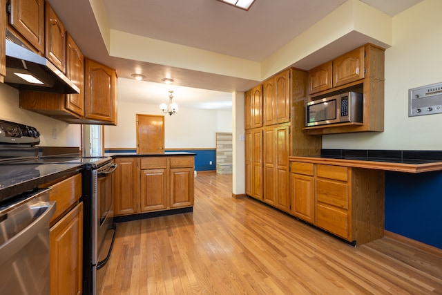 kitchen with kitchen peninsula, a chandelier, stainless steel appliances, light hardwood / wood-style floors, and decorative light fixtures