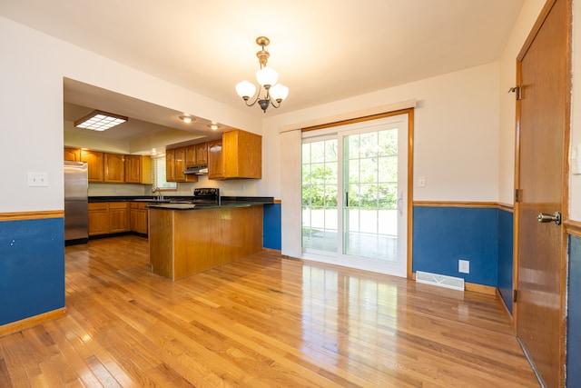 kitchen with black stove, kitchen peninsula, a notable chandelier, stainless steel refrigerator, and light hardwood / wood-style flooring