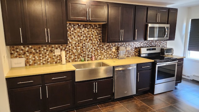 kitchen featuring dark brown cabinets, tasteful backsplash, stainless steel appliances, dark tile flooring, and sink