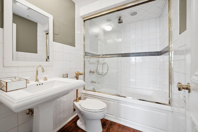 full bathroom with toilet, bath / shower combo with glass door, wood finished floors, and tile walls
