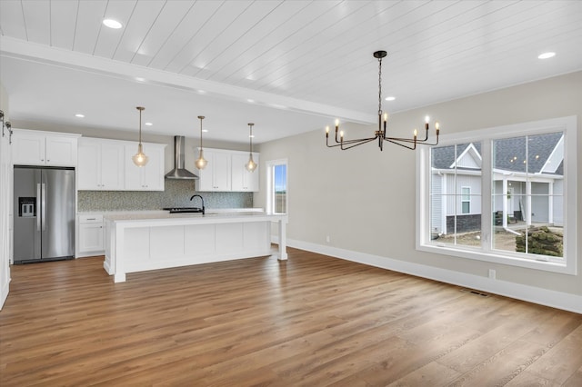 kitchen with stainless steel refrigerator with ice dispenser, wood-type flooring, wall chimney range hood, and pendant lighting