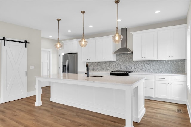 kitchen with wall chimney range hood, stainless steel fridge with ice dispenser, light hardwood / wood-style flooring, a barn door, and tasteful backsplash