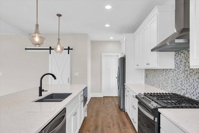 kitchen with wall chimney range hood, appliances with stainless steel finishes, wood-type flooring, a barn door, and tasteful backsplash