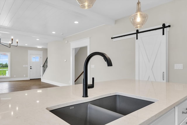 kitchen featuring light stone countertops, beam ceiling, a barn door, sink, and hardwood / wood-style flooring