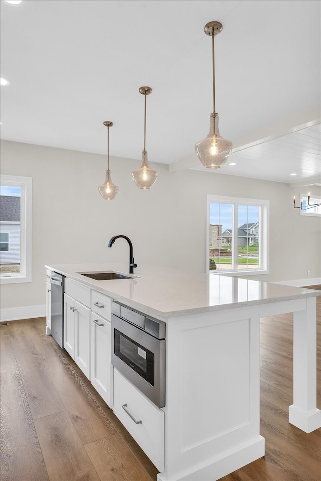 kitchen with decorative light fixtures, sink, hardwood / wood-style flooring, and a center island with sink