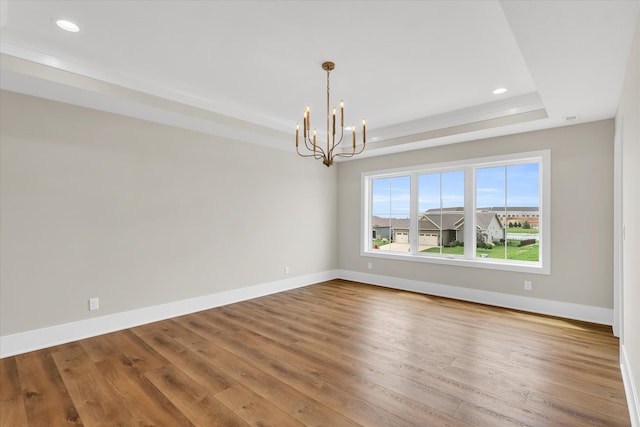 empty room with an inviting chandelier, wood-type flooring, and a raised ceiling