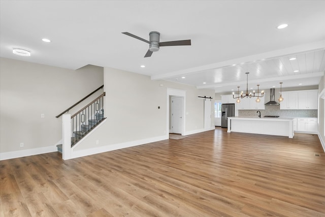 unfurnished living room with a barn door, light hardwood / wood-style floors, sink, and ceiling fan with notable chandelier