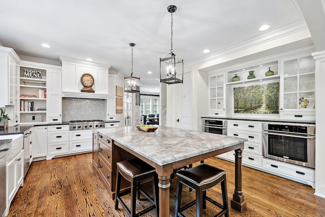 kitchen featuring a center island, white cabinetry, appliances with stainless steel finishes, a breakfast bar area, and light stone counters