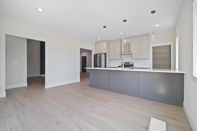 kitchen featuring appliances with stainless steel finishes, decorative light fixtures, light wood-type flooring, and wall chimney range hood