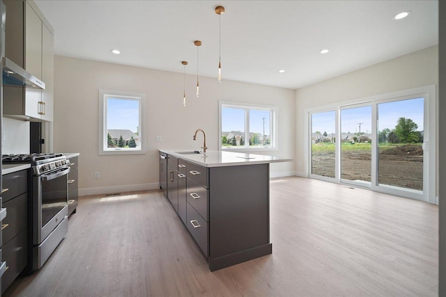 kitchen with sink, a center island with sink, light wood-type flooring, stainless steel range with gas stovetop, and pendant lighting