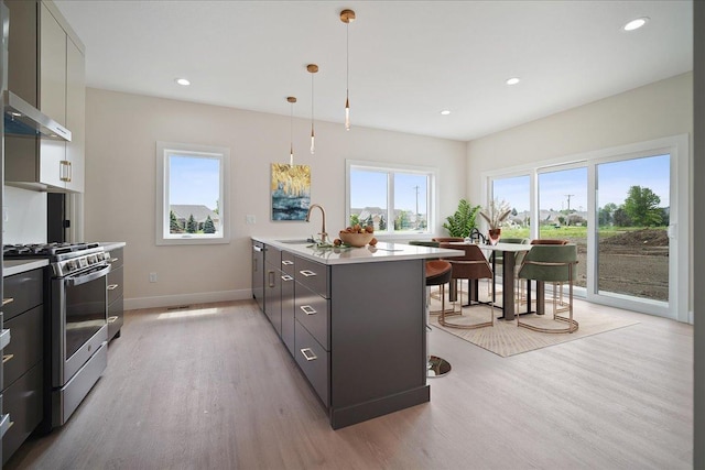 kitchen featuring decorative light fixtures, sink, stainless steel range with gas stovetop, a center island with sink, and wall chimney exhaust hood