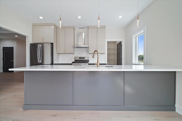 kitchen featuring wall chimney range hood, sink, appliances with stainless steel finishes, hanging light fixtures, and light hardwood / wood-style floors