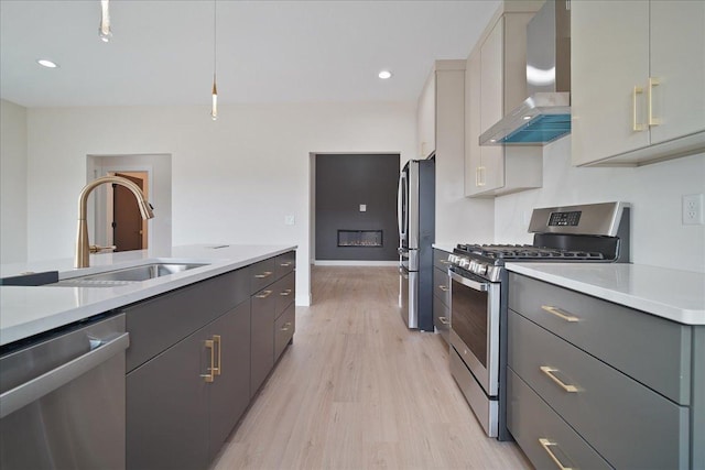 kitchen with sink, gray cabinetry, stainless steel appliances, light hardwood / wood-style floors, and wall chimney exhaust hood