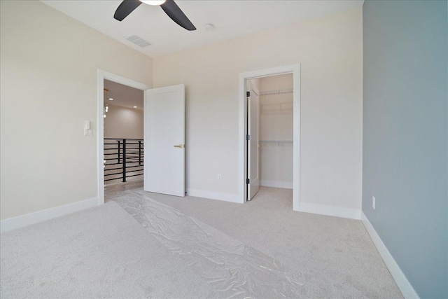 unfurnished bedroom featuring ceiling fan, a walk in closet, a closet, and light carpet