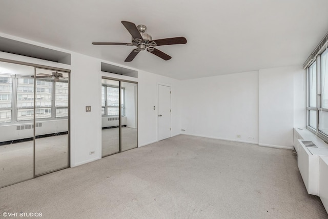 unfurnished bedroom featuring radiator, multiple windows, multiple closets, and light colored carpet