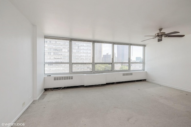 spare room with baseboards, a ceiling fan, light colored carpet, radiator, and a view of city