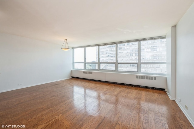 spare room with baseboard heating, radiator, baseboards, and wood finished floors