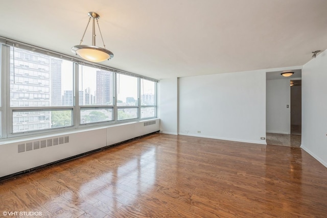 empty room with baseboards, baseboard heating, a city view, and wood finished floors