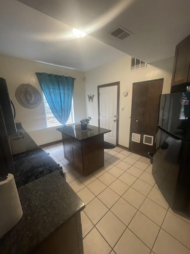 kitchen featuring black fridge, light tile patterned flooring, dark brown cabinets, and a center island