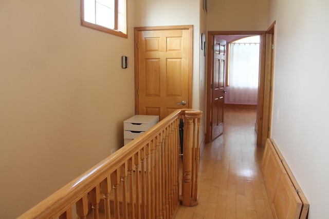 hallway with a baseboard radiator, an upstairs landing, and light wood-style flooring