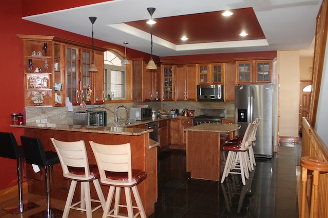 kitchen with appliances with stainless steel finishes, a tray ceiling, decorative light fixtures, light stone counters, and kitchen peninsula