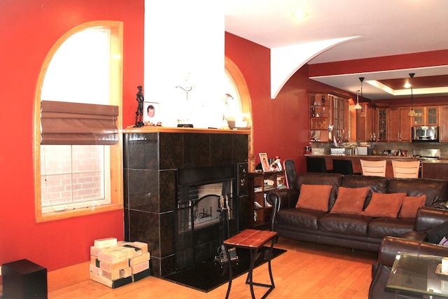 living room featuring a raised ceiling, a tile fireplace, and light hardwood / wood-style flooring