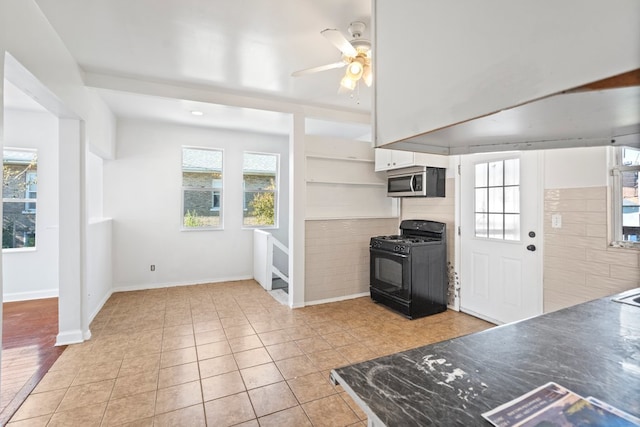 kitchen with black gas range, ceiling fan, light tile patterned floors, white cabinets, and tile walls