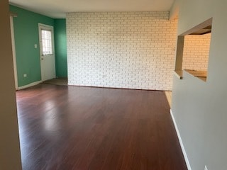 unfurnished room with dark wood-type flooring and brick wall