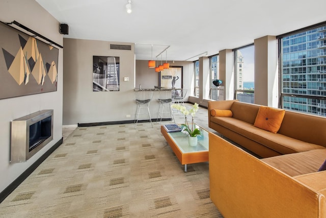 living area featuring light colored carpet, visible vents, baseboards, a glass covered fireplace, and rail lighting