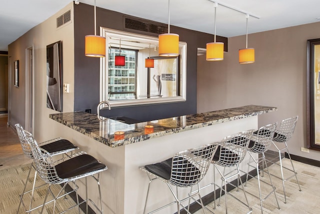 kitchen featuring visible vents, dark stone counters, a kitchen breakfast bar, decorative light fixtures, and a peninsula