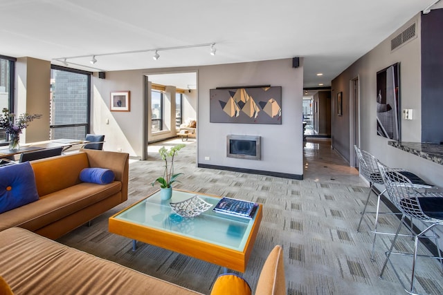 living room featuring light colored carpet, a glass covered fireplace, visible vents, and baseboards