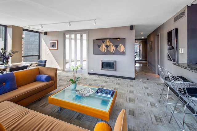 living area featuring light carpet, a glass covered fireplace, visible vents, and baseboards