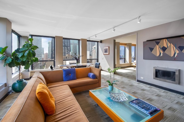 carpeted living room featuring a view of city, baseboards, a glass covered fireplace, and a healthy amount of sunlight