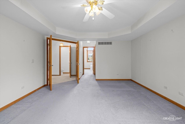 carpeted empty room with ceiling fan and a tray ceiling