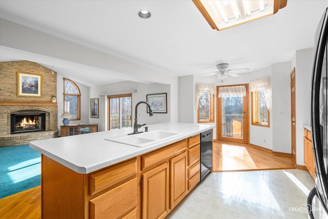 kitchen featuring ceiling fan, dishwasher, sink, a brick fireplace, and an island with sink