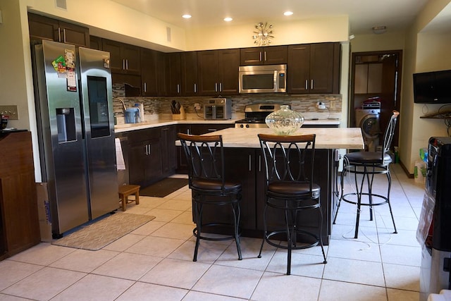 kitchen with tasteful backsplash, light countertops, appliances with stainless steel finishes, a kitchen island, and dark brown cabinetry