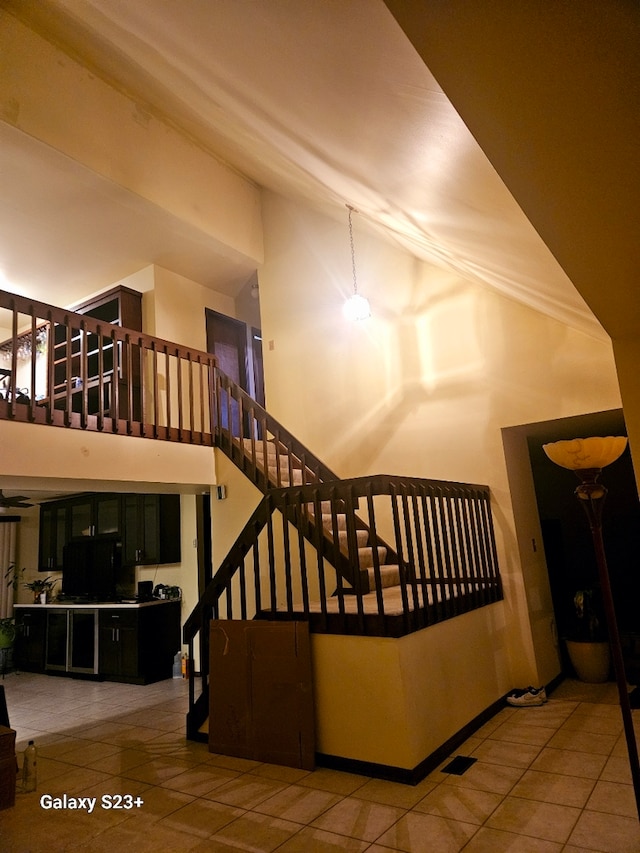 staircase featuring high vaulted ceiling and tile patterned floors