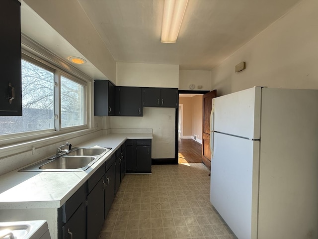 kitchen featuring light floors, freestanding refrigerator, a sink, light countertops, and dark cabinets