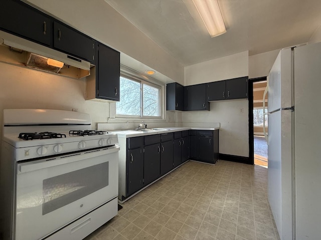 kitchen featuring under cabinet range hood, white appliances, and dark cabinetry