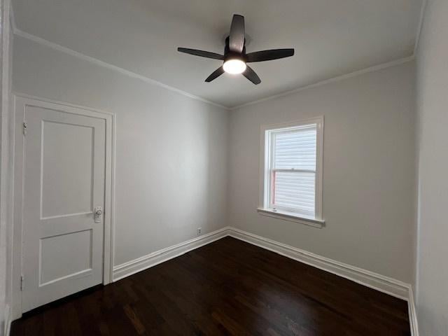 empty room featuring dark wood-type flooring, crown molding, a ceiling fan, and baseboards